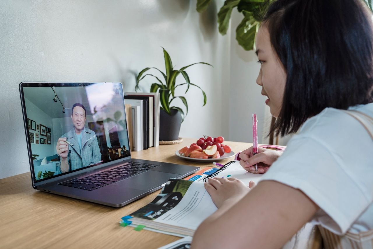 why-choose-us Young girl engaged in online learning via video call, studying with laptop and notes.