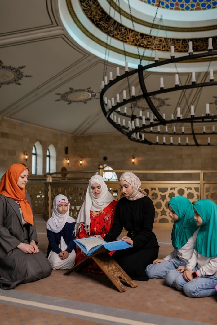 Services-03 A Muslim family, including women and girls, gather for prayer in a beautifully adorned mosque.